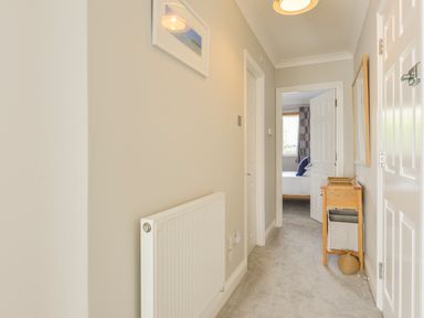 A hallway with a radiator a small wooden table with a basket and a mirror and a bedroom visible at 3 Tarifa in Bigbury-on-Sea
