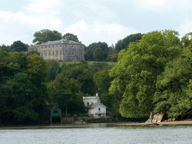 A large stone house on a hill surrounded by trees and a white house near a river at The Bathing House in Ashprington