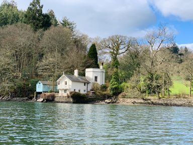 A house with a blue cabin by the water surrounded by trees and greenery at The Bathing House in Ashprington