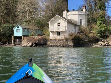 A kayak on a body of water facing two houses near trees at The Bathing House in Ashprington