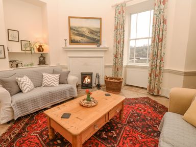 A sitting room with sofas a wooden coffee table a red patterned rug a fireplace and floral curtains at The Bathing House in Ashprington