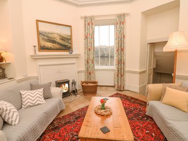 A living room with two sofas and a wooden coffee table in front of a fireplace with a fire burning at The Bathing House in Ashprington