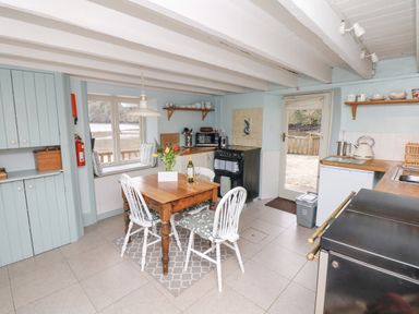 A kitchen with a wooden table and four chairs a window seat stove and door to outside at The Bathing House in Ashprington