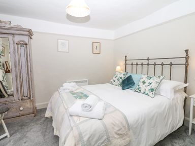 A bedroom with a bed with pillows and towels and a wooden wardrobe with a mirror at The Bathing House in Ashprington