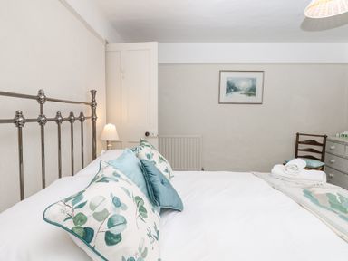 A bedroom with a bed with floral and blue pillows a lamp a chair a dresser and a framed picture on the wall at The Bathing House in Ashprington