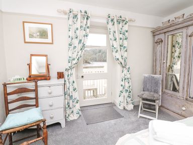 A bedroom with wooden chairs a white dresser with a mirror floral curtains and a wooden wardrobe with a mirror at The Bathing House in Ashprington