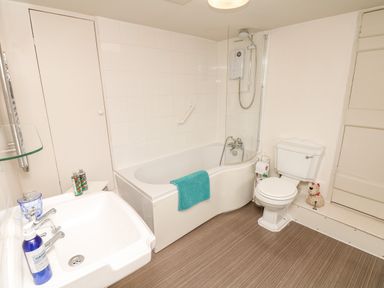 A bathroom with a sink, bathtub with shower, toilet, and storage cupboard at The Bathing House in Ashprington