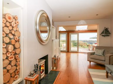 A living room with a fireplace logs stacked in a niche and glass doors leading to a patio with outdoor furniture at Dove Cottage in Dittisham