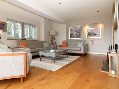 A living room with gray sofas orange and gray pillows a coffee table floor lamp paintings on the wall and wooden flooring at Dove Cottage in Dittisham