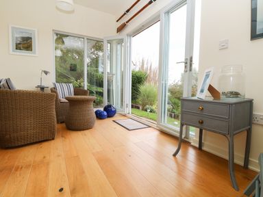 A sitting area with wicker chairs and a table next to sliding glass doors leading to a garden at Dove Cottage in Dittisham