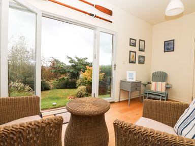 A room with wicker chairs and table looking out through glass doors to a garden at Dove Cottage in Dittisham