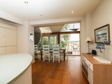 A dining area with wooden table and chairs next to large glass doors and windows with a sideboard and a lamp in Dove Cottage in Dittisham