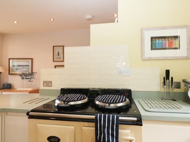 A kitchen countertop with a stove covered by lids and a striped cloth at Dove Cottage in Dittisham