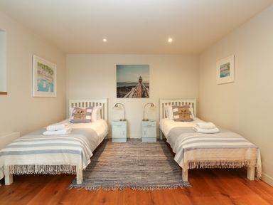 A bedroom with two single beds with striped blankets and pillows separated by two small blue nightstands with lamps and wall art at Dove Cottage in Dittisham