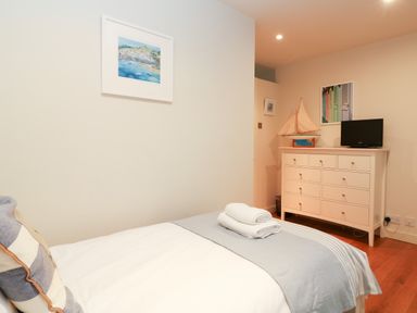 A bedroom with a bed with folded towels on it and a white dresser with a model sailboat and a TV on top at Dove Cottage in Dittisham