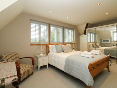A bedroom with a bed with pillows and folded towels bedside tables with lamps striped chair and mirrored wardrobe at Dove Cottage in Dittisham