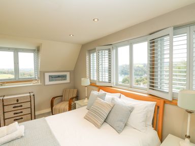 A bedroom with a bed with pillows a striped armchair a chest of drawers and windows with shutters at Dove Cottage in Dittisham