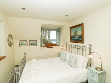 A bedroom with a double bed white linens and striped pillows two bedside tables with lamps and framed paintings on the walls at Dove Cottage in Dittisham