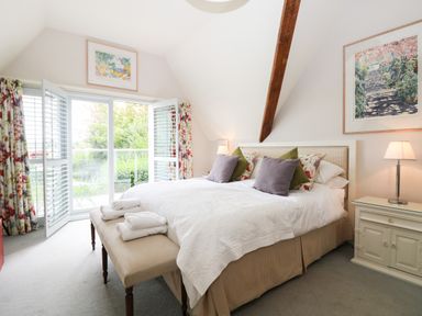 A bedroom with a bed with pillows and folded towels a bench at the foot of the bed two bedside tables with lamps floral curtains and sliding glass doors at Dove Cottage in Dittisham