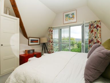 A bedroom with a bed pillows red chest tripod lamp framed pictures and floral curtains at Dove Cottage in Dittisham
