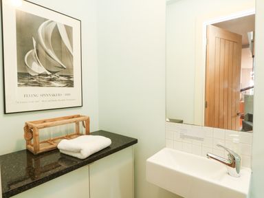 A bathroom corner with a sink a mirror a wooden framed picture of a sailboat and a black countertop with a towel and wooden container at Dove Cottage in Dittisham