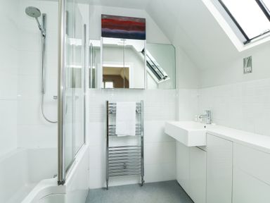 A bathroom with a bathtub and shower, a towel rail with towel, a sink, mirror cabinets, and a skylight window at Dove Cottage in Dittisham