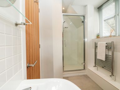 A bathroom with a glass shower enclosure a wooden door and a towel on a metal radiator at Dove Cottage in Dittisham