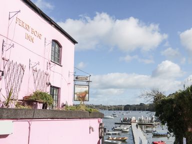 A pink building with a sign reading Ferry Boat Inn next to a dock with boats on a river at Dove Cottage in Dittisham