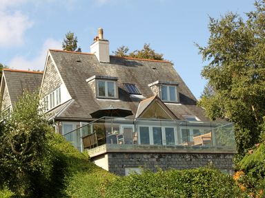 A house with a balcony surrounded by trees and bushes at Dove Cottage in Dittisham