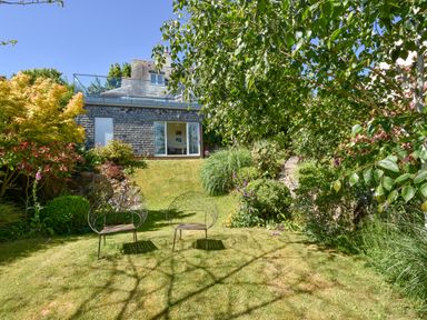 A garden with two metal chairs on grass and a house with a glass door in the background at Dove Cottage in Dittisham