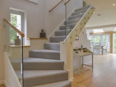 A staircase with grey carpet and wooden handrails next to a window with lanterns and a small desk in a room with wooden floors at Dove Cottage in Dittisham
