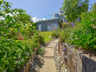 A garden path with stone slabs and plants leading to a house at Dove Cottage in Dittisham