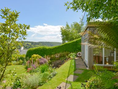 A garden with lawn and plants next to a building with glass doors at Dove Cottage in Dittisham