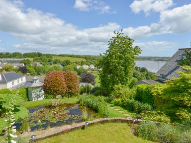 A garden with a pond and various trees overlooking houses and a body of water at Dove Cottage in Dittisham