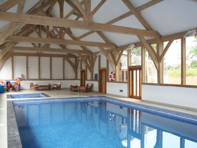 An indoor swimming pool with wooden beams and seating area at Oak Tree in Halwell