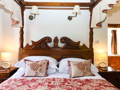 A bedroom with a decorated wooden bed and bedside lamps at Oak Tree in Halwell