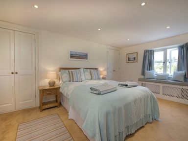 A bedroom with a double bed with folded towels bedside tables lamps built in wardrobes and a window seat with cushions at Junket Cottage in Noss Mayo