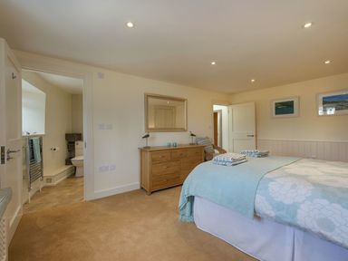 A bedroom with a double bed blue bedding dresser with mirror and an open door to a bathroom at Junket Cottage in Noss Mayo