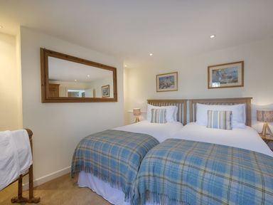 A bedroom with two single beds with blue plaid blankets at Junket Cottage in Noss Mayo