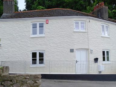 The exterior of a white stone cottage with multiple windows a door and a metal railing in front at Junket Cottage in Noss Mayo