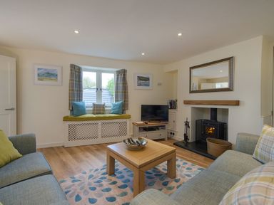 A living room with two sofas a wooden coffee table a fireplace and a window seat at Junket Cottage in Noss Mayo