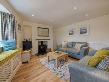 A living room with sofas a coffee table a fireplace and a window seat at Junket Cottage in Noss Mayo