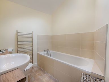 A bathroom with a bathtub sink toilet towel rack and wicker basket at Junket Cottage in Noss Mayo