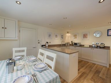 A kitchen with dining table set with plates and cutlery at Junket Cottage in Noss Mayo