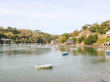 A river with boats moored near a shoreline with trees and houses at Junket Cottage in Noss Mayo