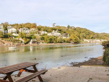 A wooden picnic table by a river with houses and trees on the opposite bank at Junket Cottage in Noss Mayo