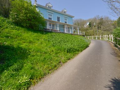 A blue two-story house with white trim on a hill next to a paved driveway and green grass at Woodlands in Dartmouth