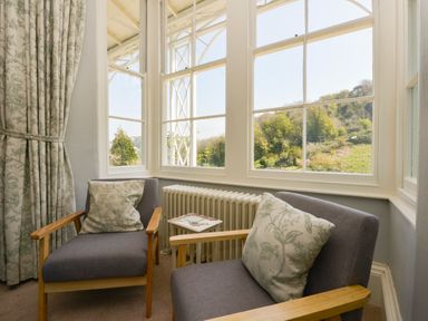 Two chairs with patterned cushions by a window with curtains and a radiator at Woodlands in Dartmouth