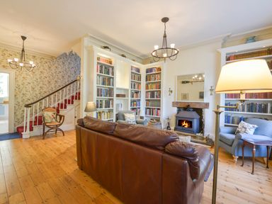 A living room with a leather sofa a fireplace built in bookshelves and floral wallpaper at Woodlands in Dartmouth