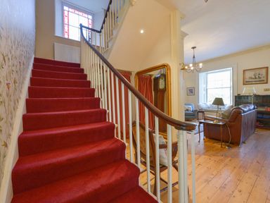 A staircase with red carpet beside a living room with sofas and wooden floor at Woodlands in Dartmouth